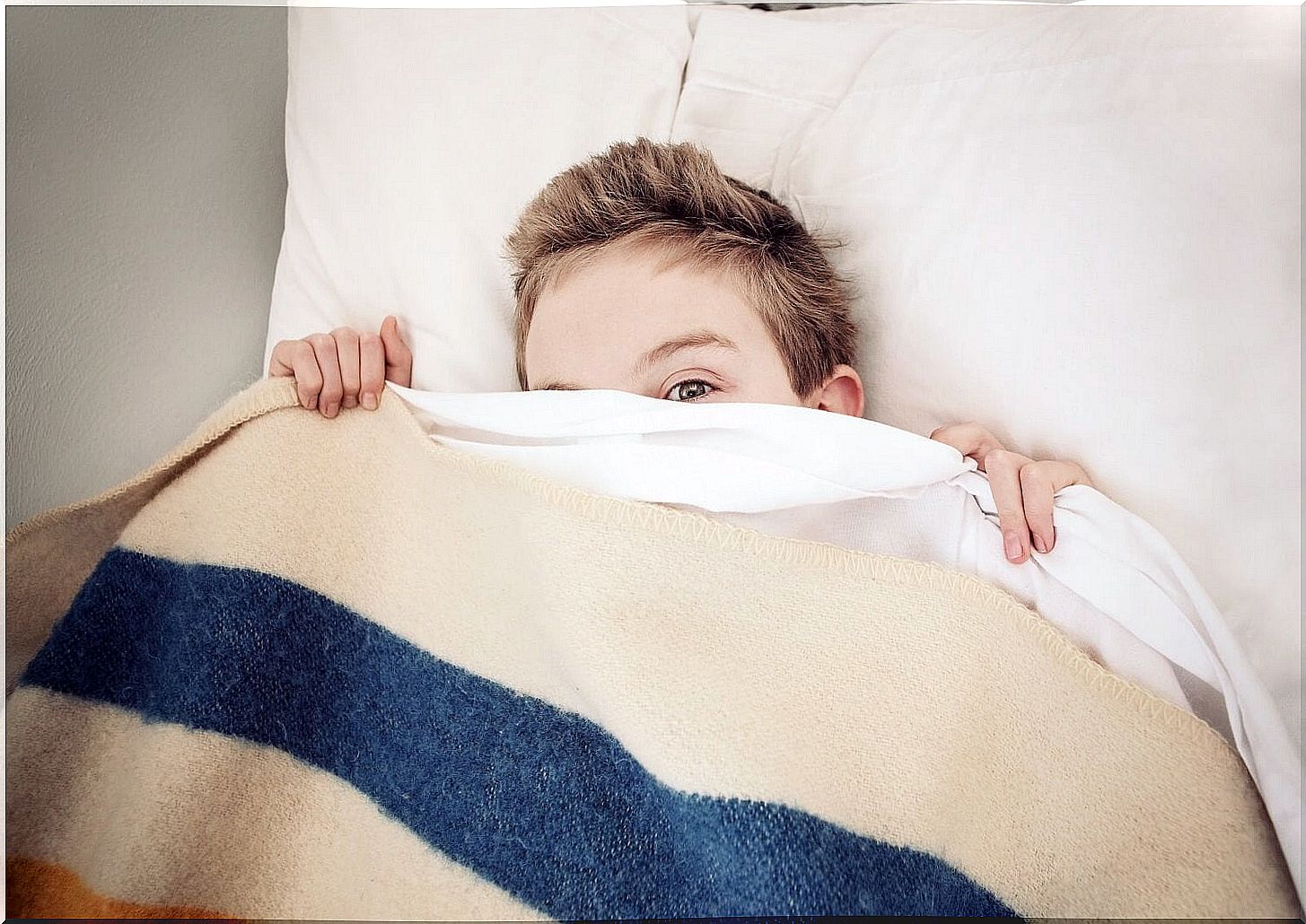 boy in bed hiding under the sheets scared